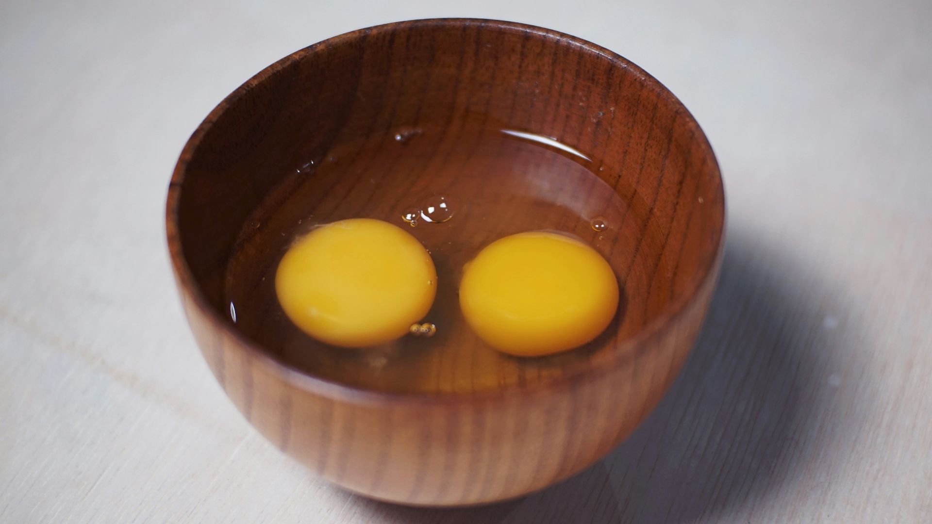 Two raw egg yolks sit in a wooden bowl.