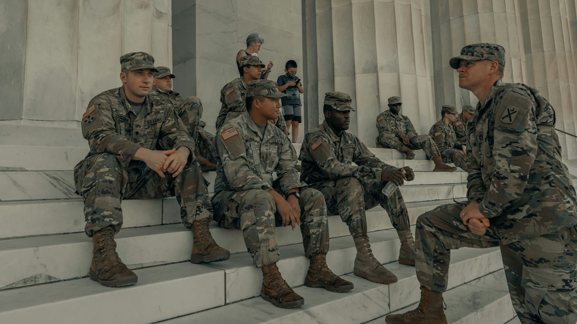 men in camouflage uniform standing near white wall