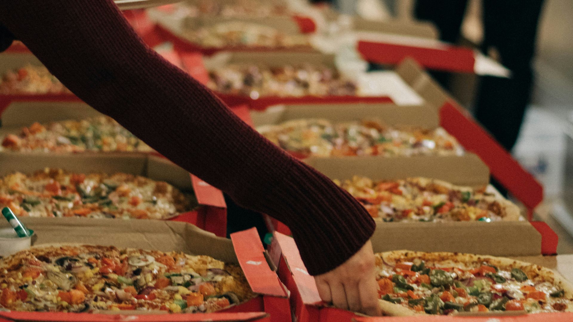 person reaching of a pizza on other side of table