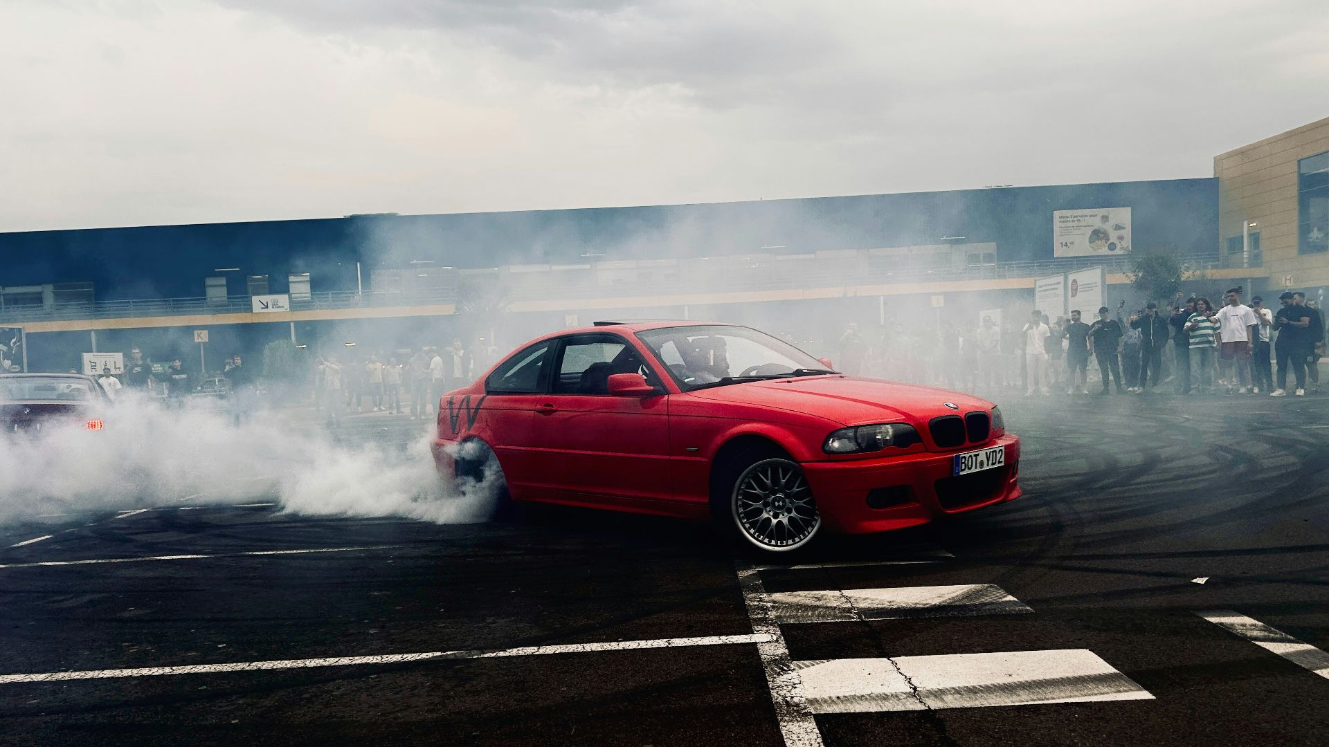 A red car driving down a street next to a crowd of people