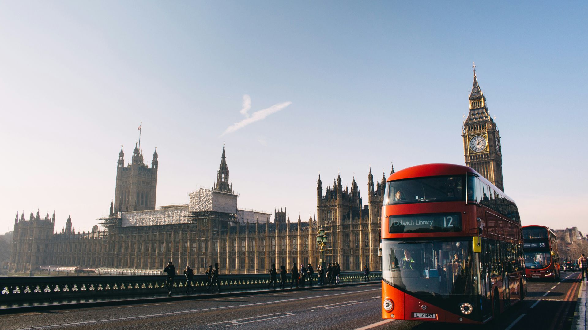 red double-decker bus passing Palace of Westminster, London during daytime