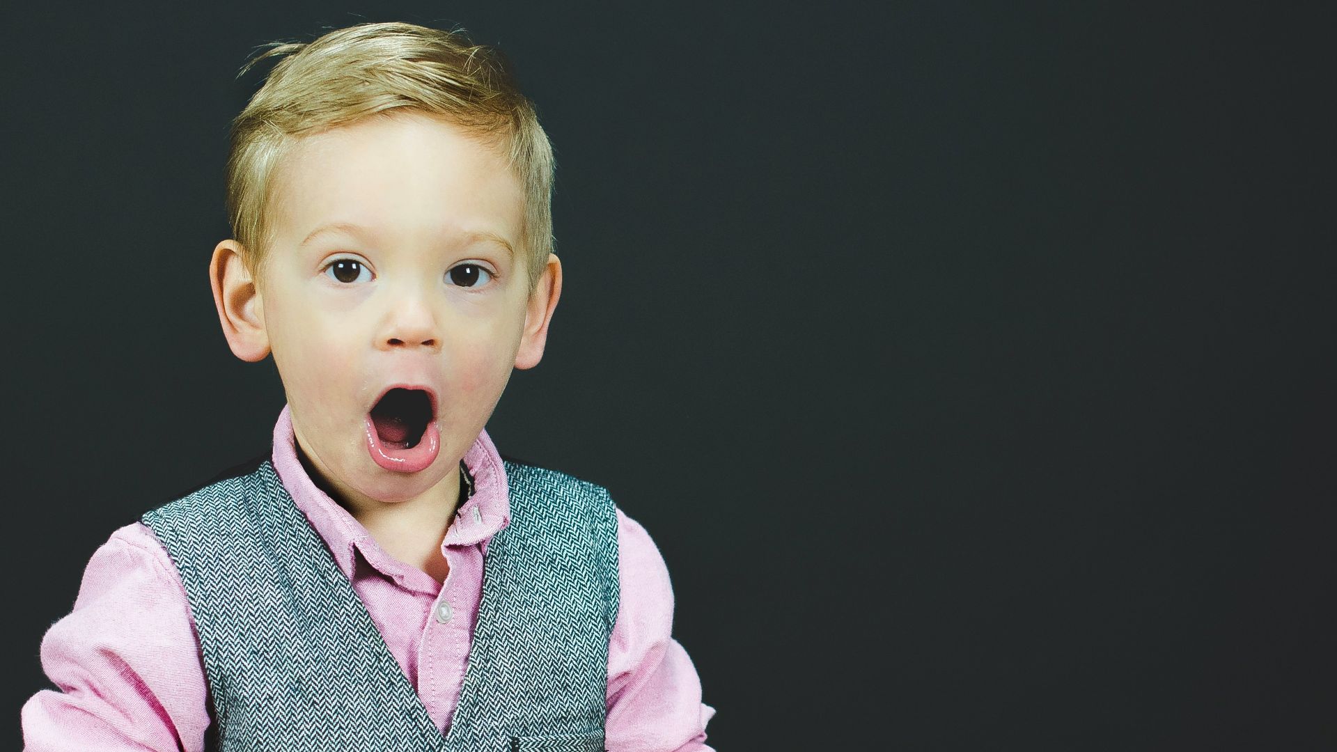 boy wearing gray vest and pink dress shirt holding book
