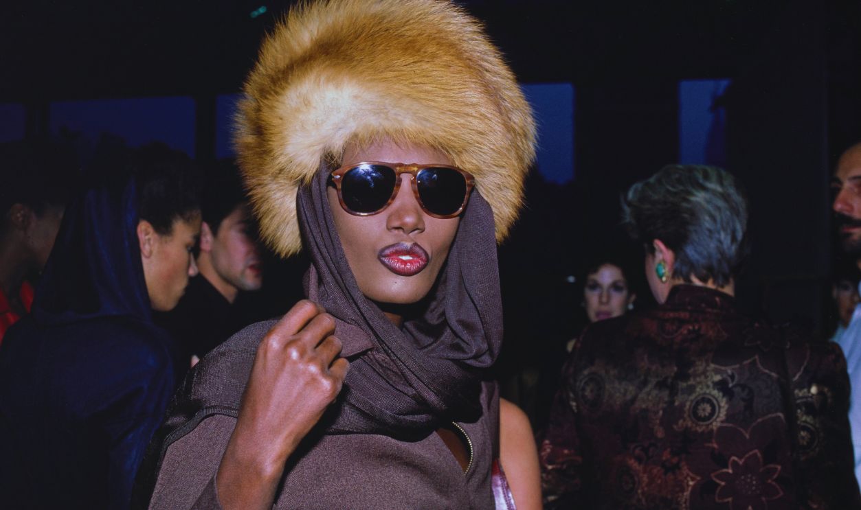 Gettyimages - 1361744711, The World's Largest Photo Session Benefit For AIDS Research Foundation Jamaican-American fashion model, singer and actress Grace Jones, wearing a brown headscarf and a fur hat, attends the World's Largest Photo Session Benefit for AIDS Research Foundation, held at the Jacob Javits Convention Center in New York City, New York, 29th April 1986.