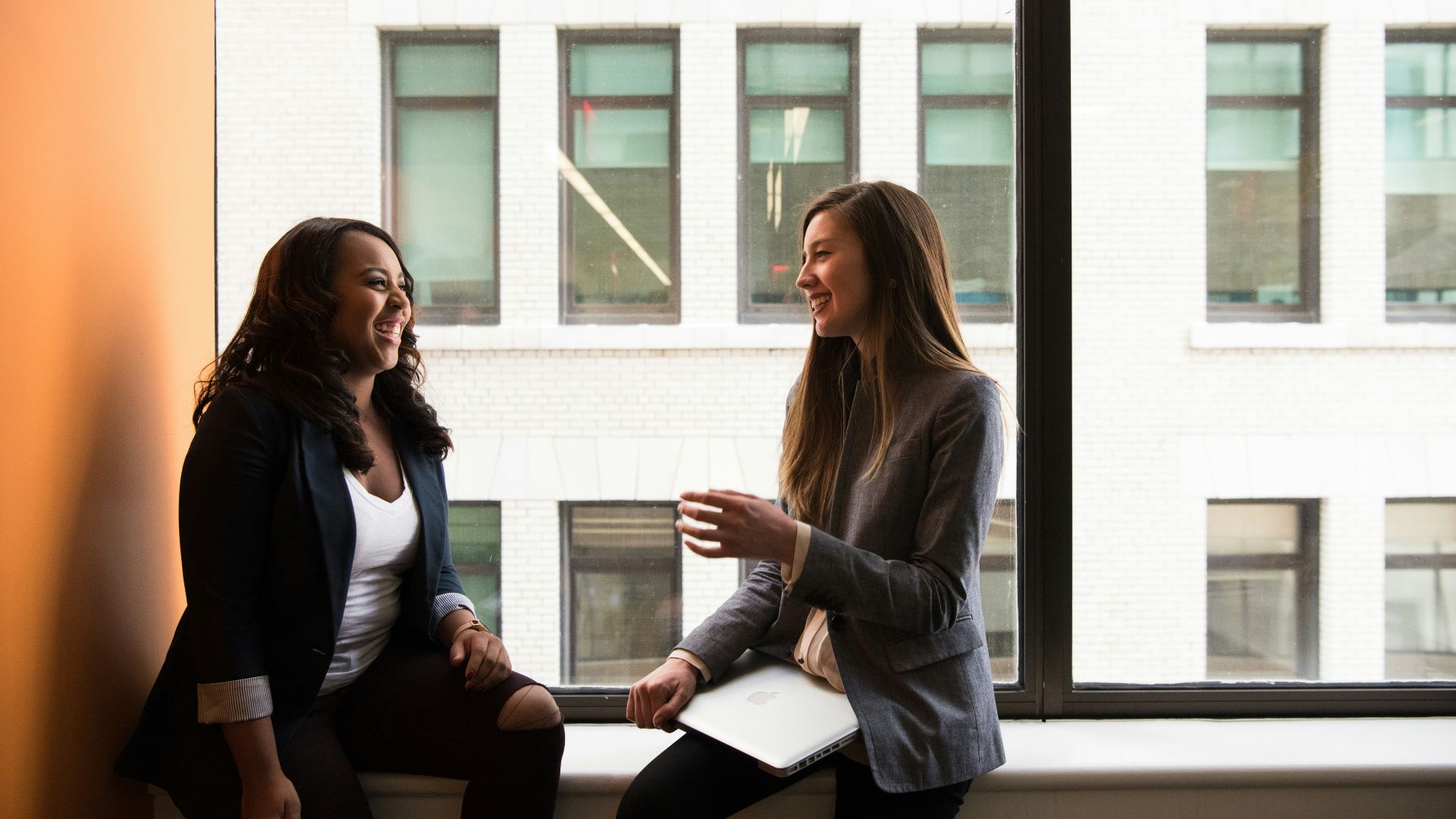 two woman sitting by the window laughing
