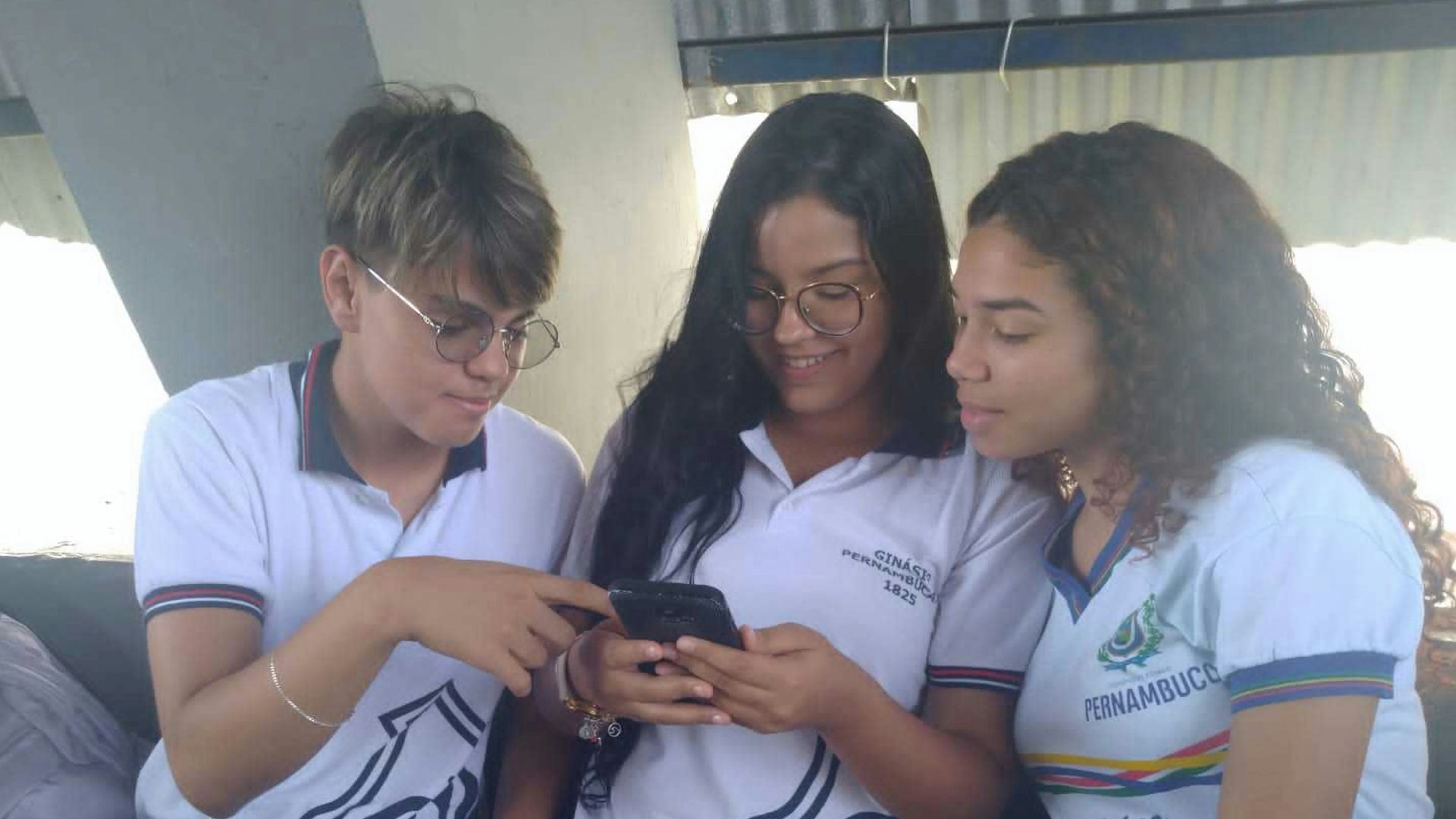 three girls sitting on a couch looking at a cell phone