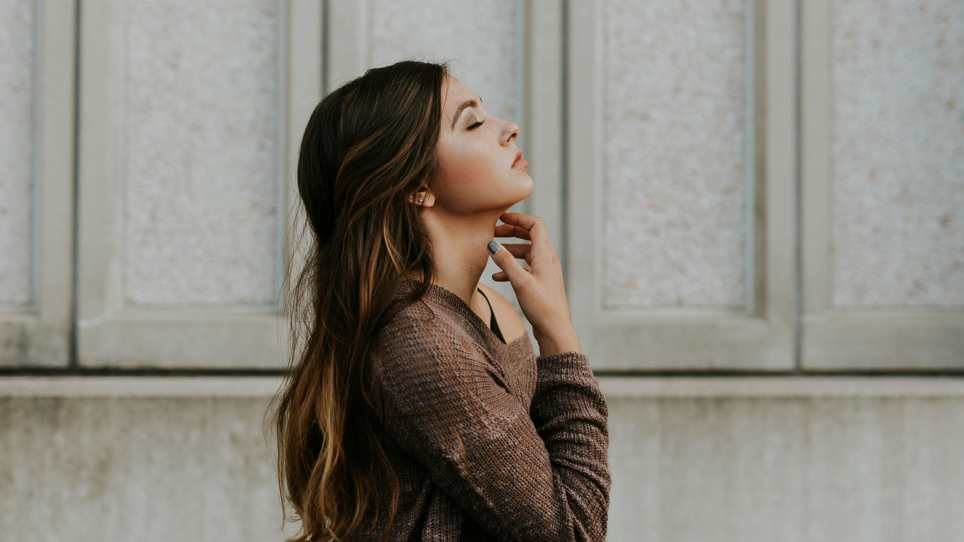 woman in brown long-sleeved top standing beside wall