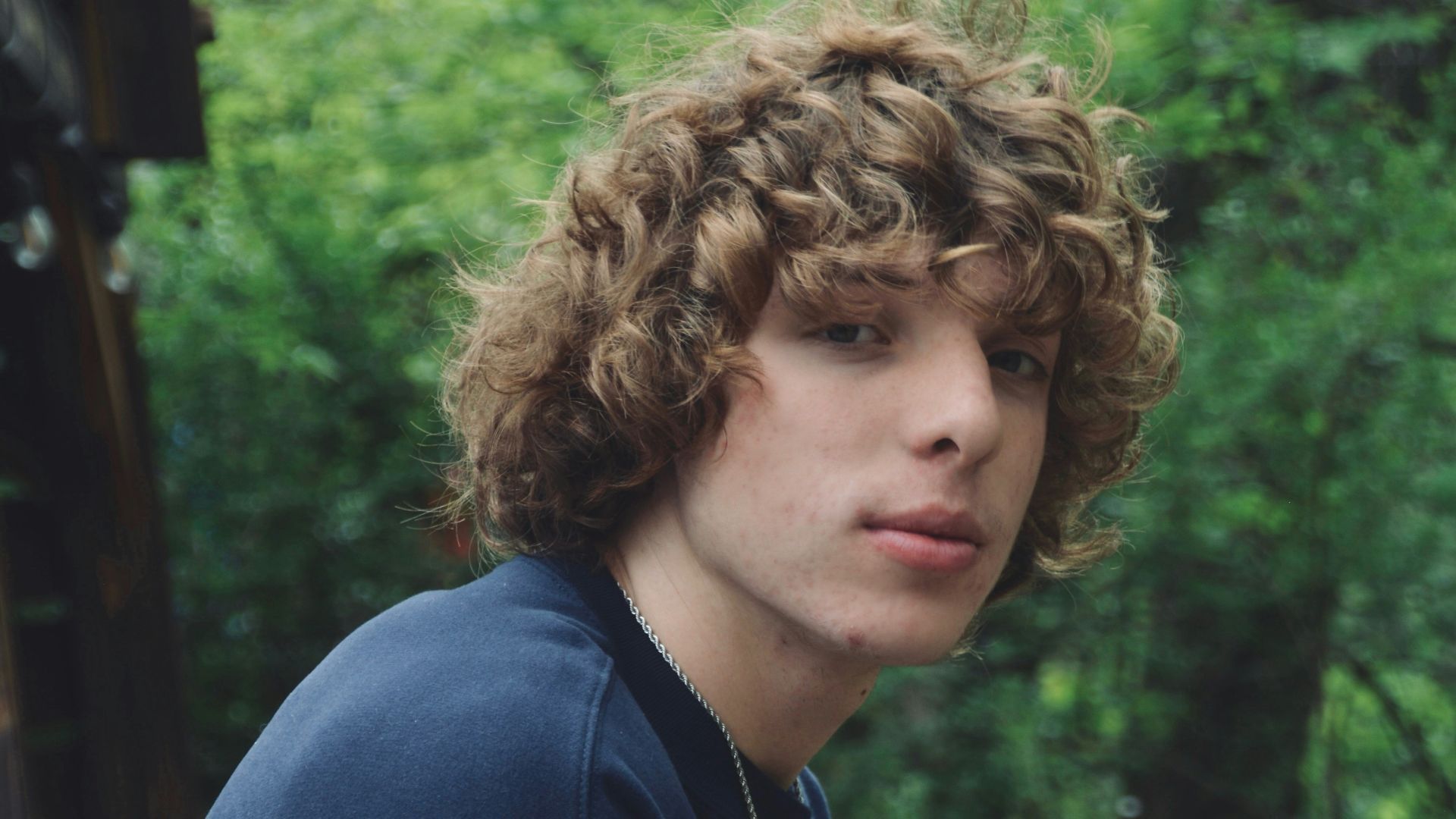 a young man with curly hair sitting on a bench