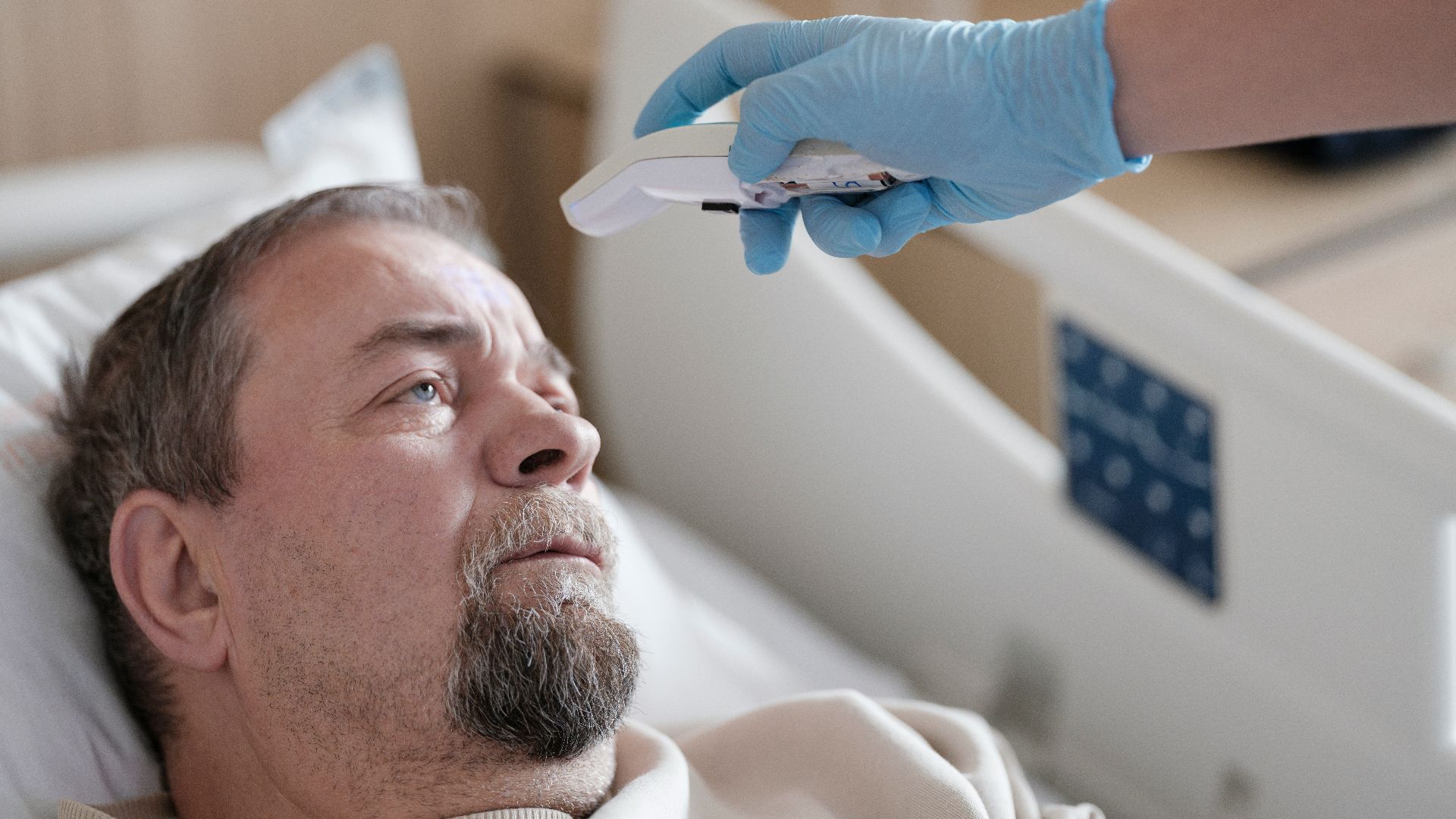 a man laying in a hospital bed with a thermometer in his hand