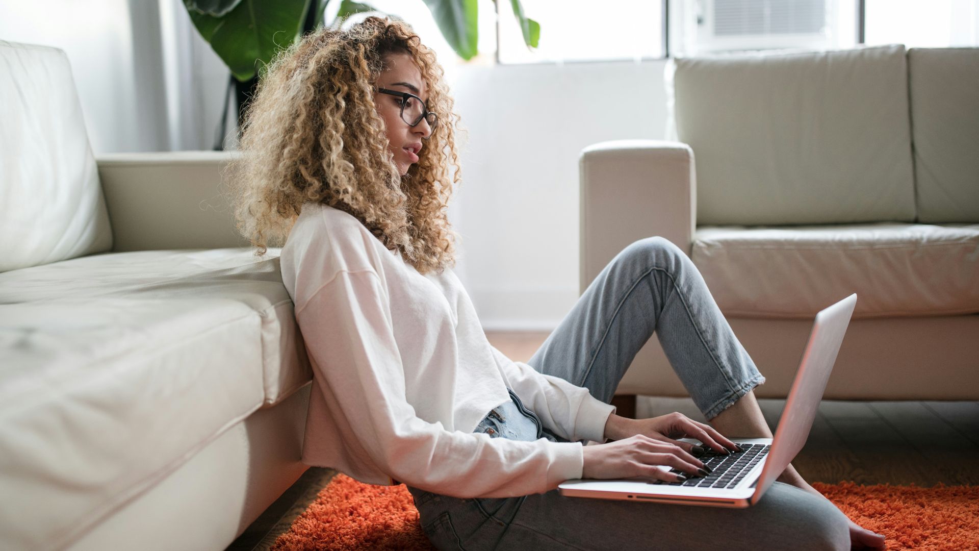 woman sitting on floor and leaning on couch using laptop