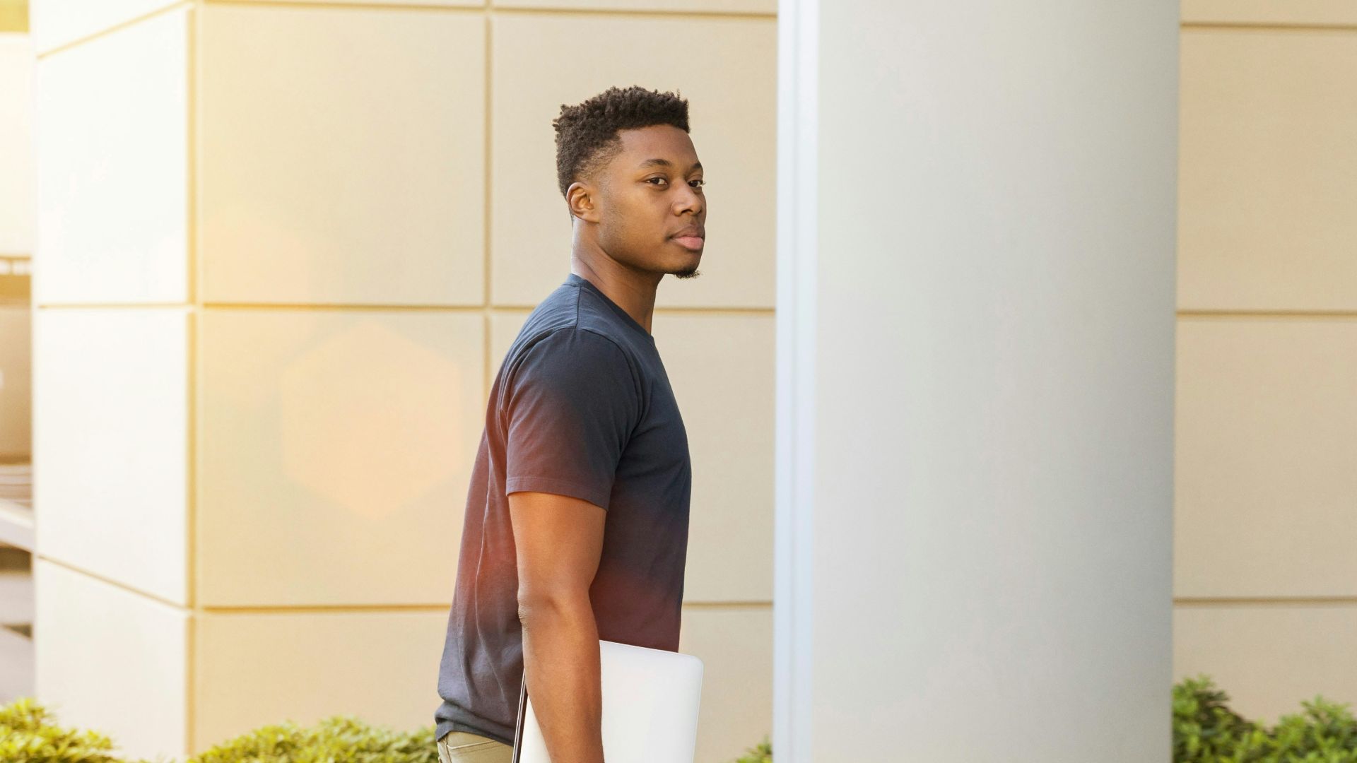 man holding laptop walking towards building