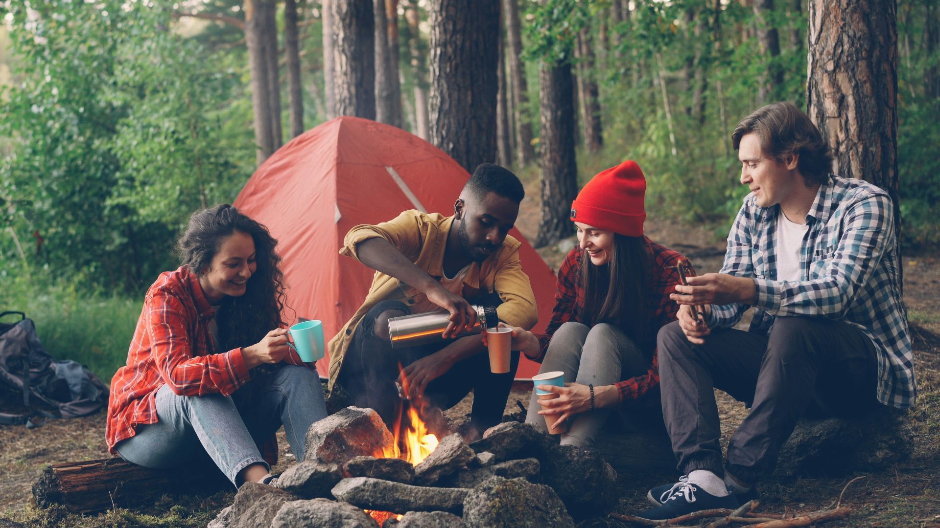 Friends gathered around campfire in forest with tent