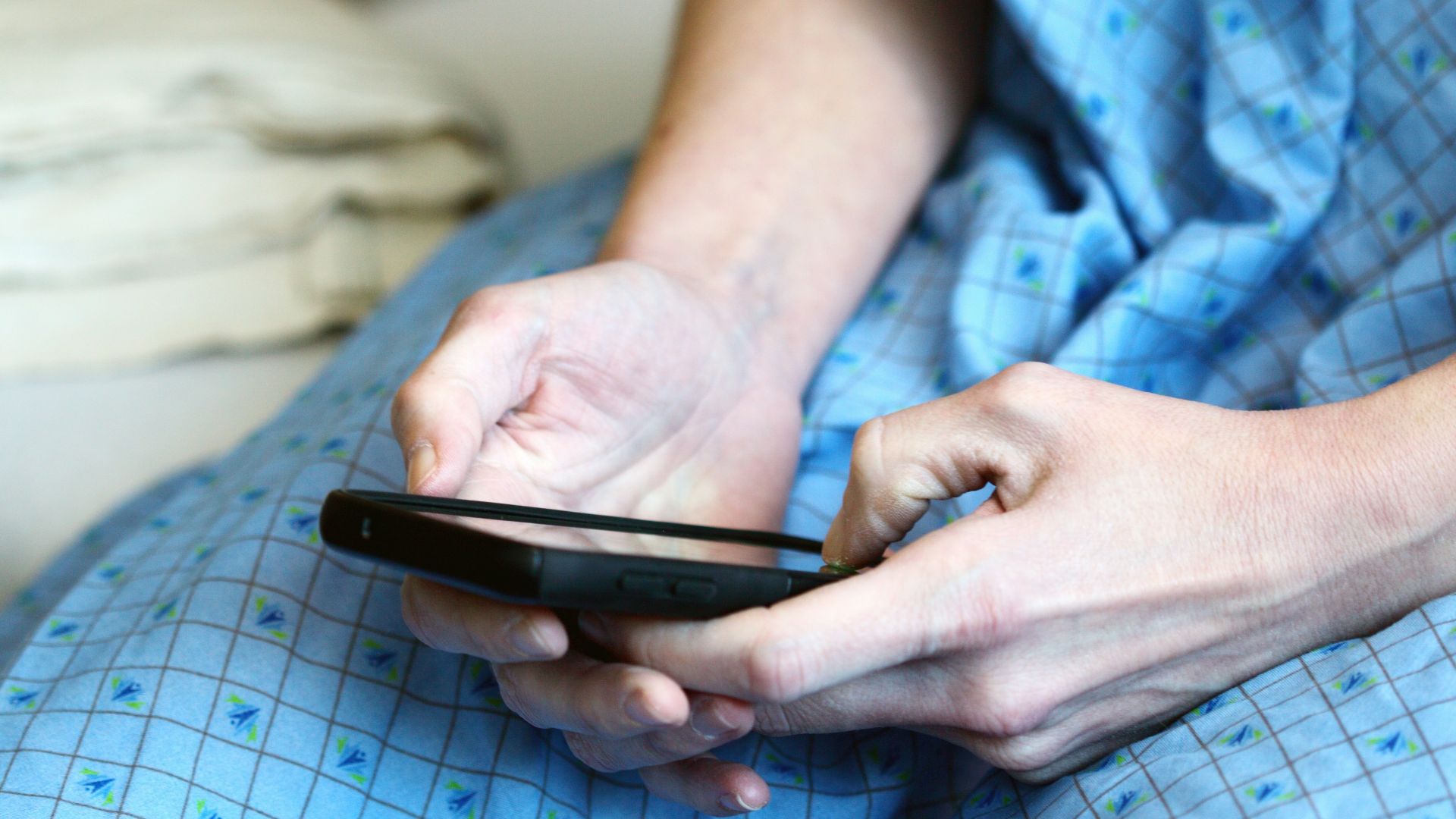 person in blue and white checkered button up shirt holding black smartphone
