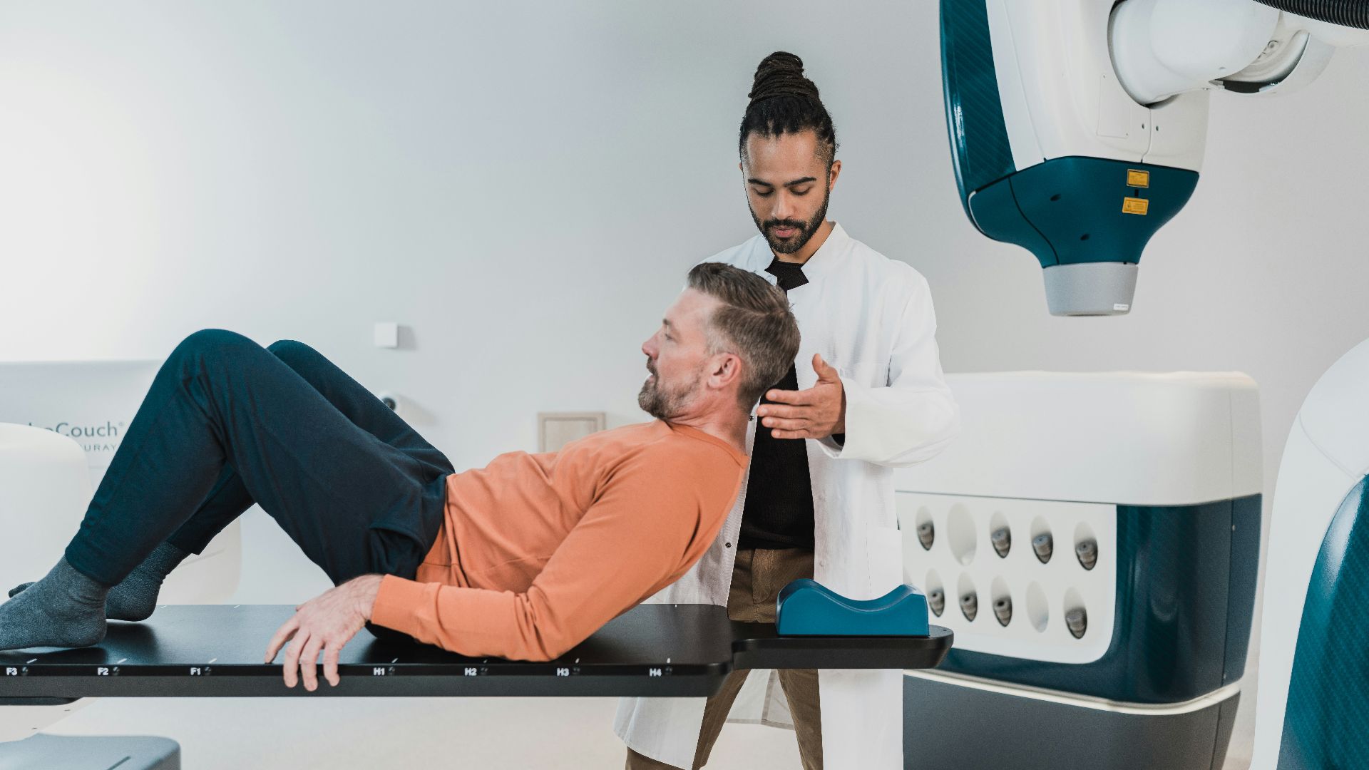 a person lying on a bed with another man standing behind him