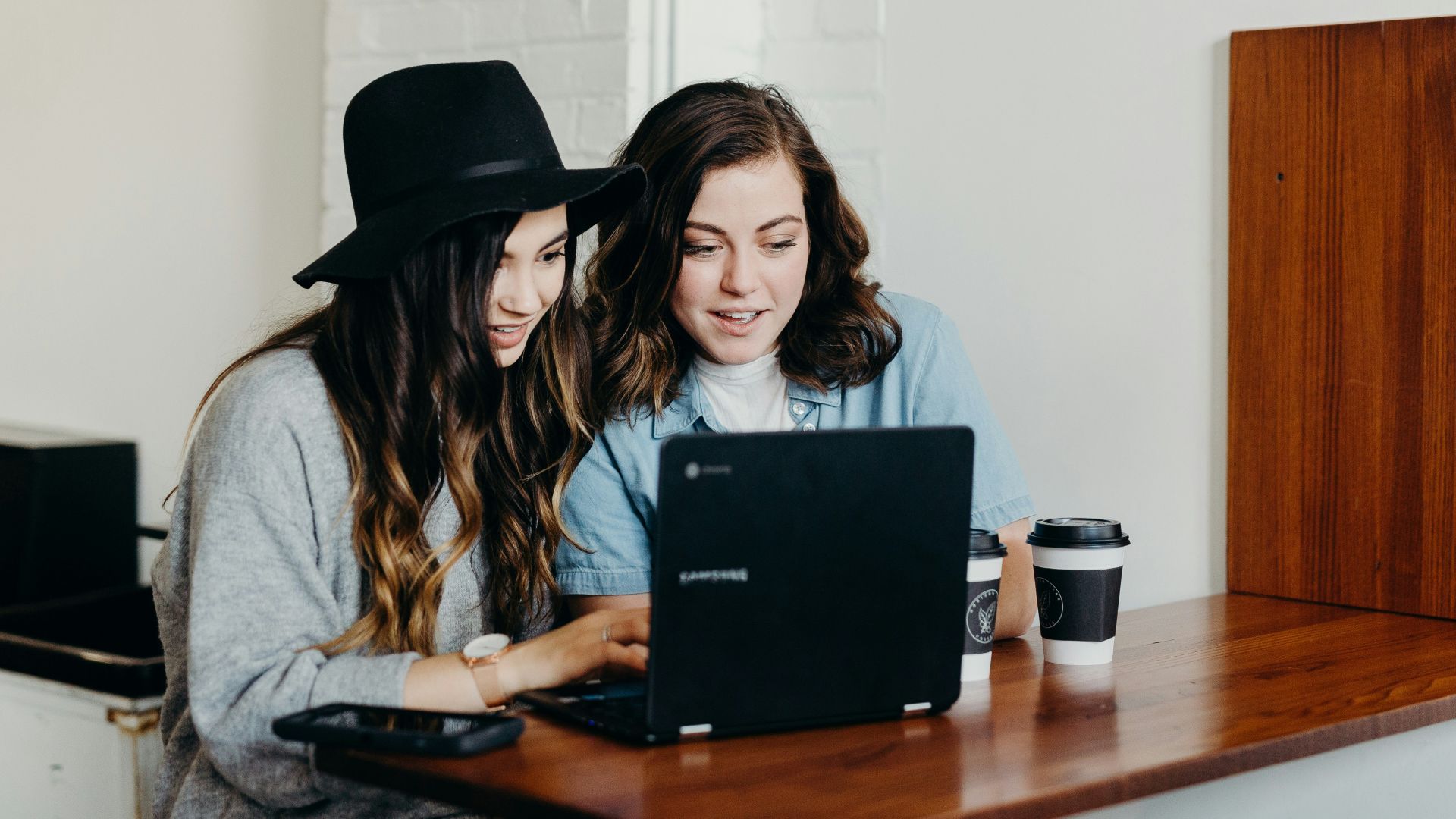 two woman sitting near table using Samsung laptop