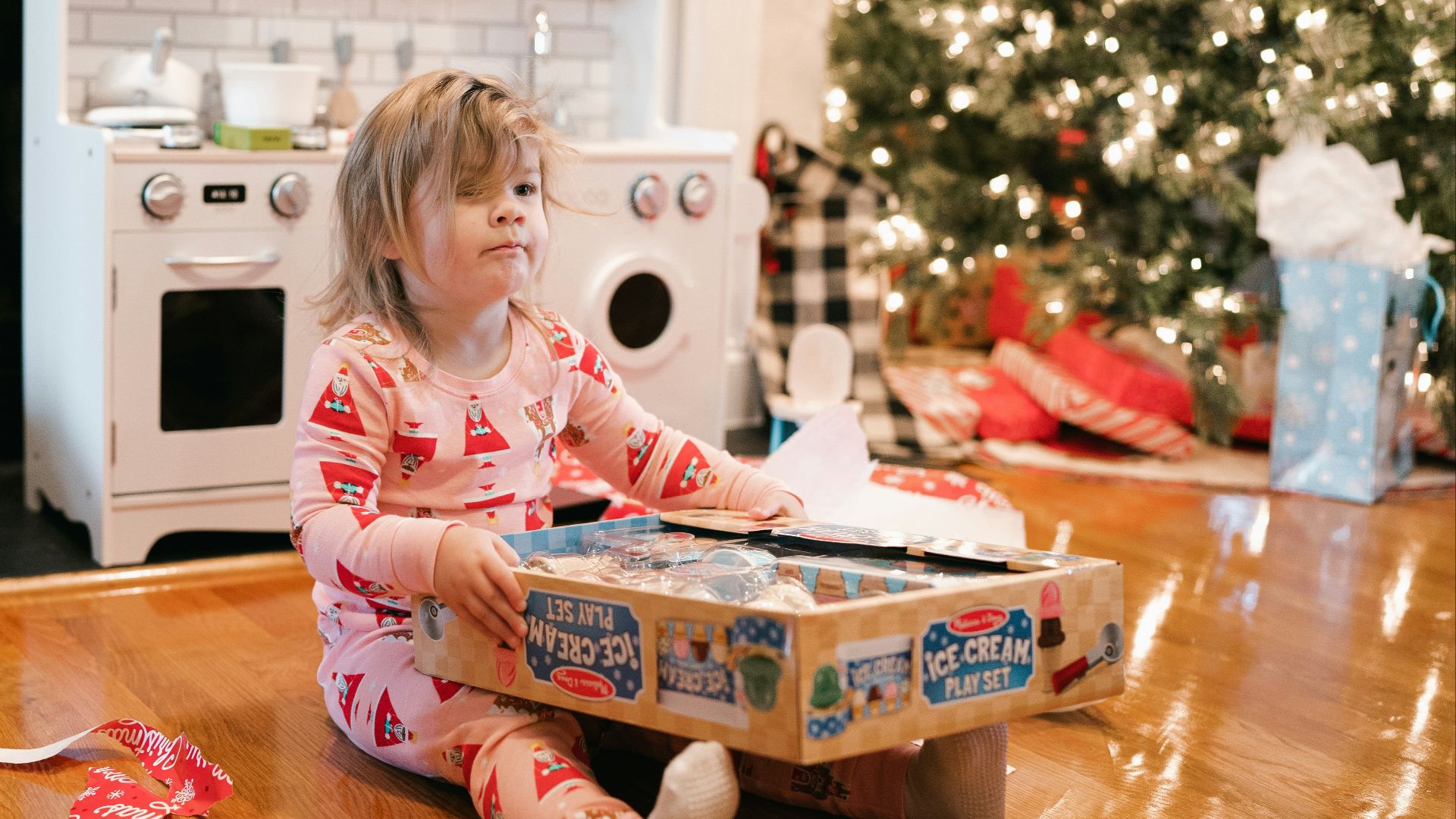 a little girl sitting on the floor in front of a christmas tree