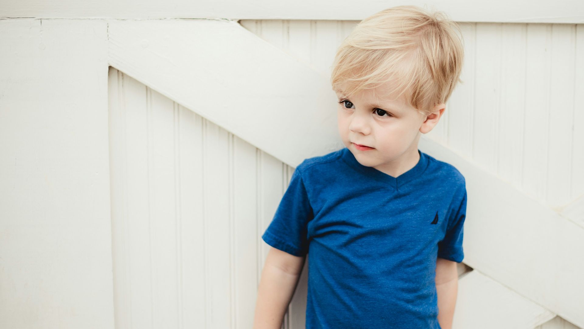 boy in blue crew neck t-shirt standing beside white wall