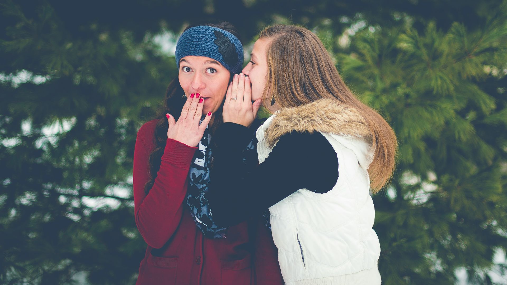 woman whispering on woman's ear while hands on lips