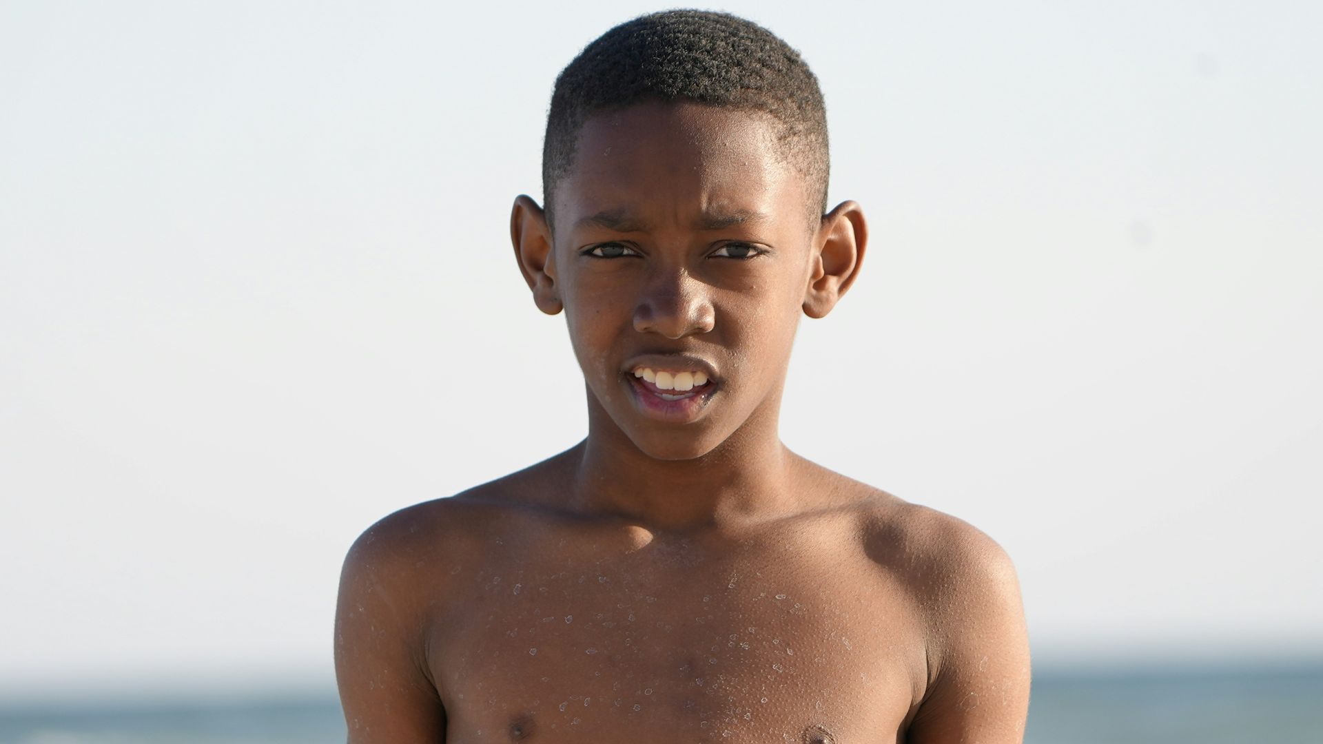 a young boy standing on a beach next to the ocean