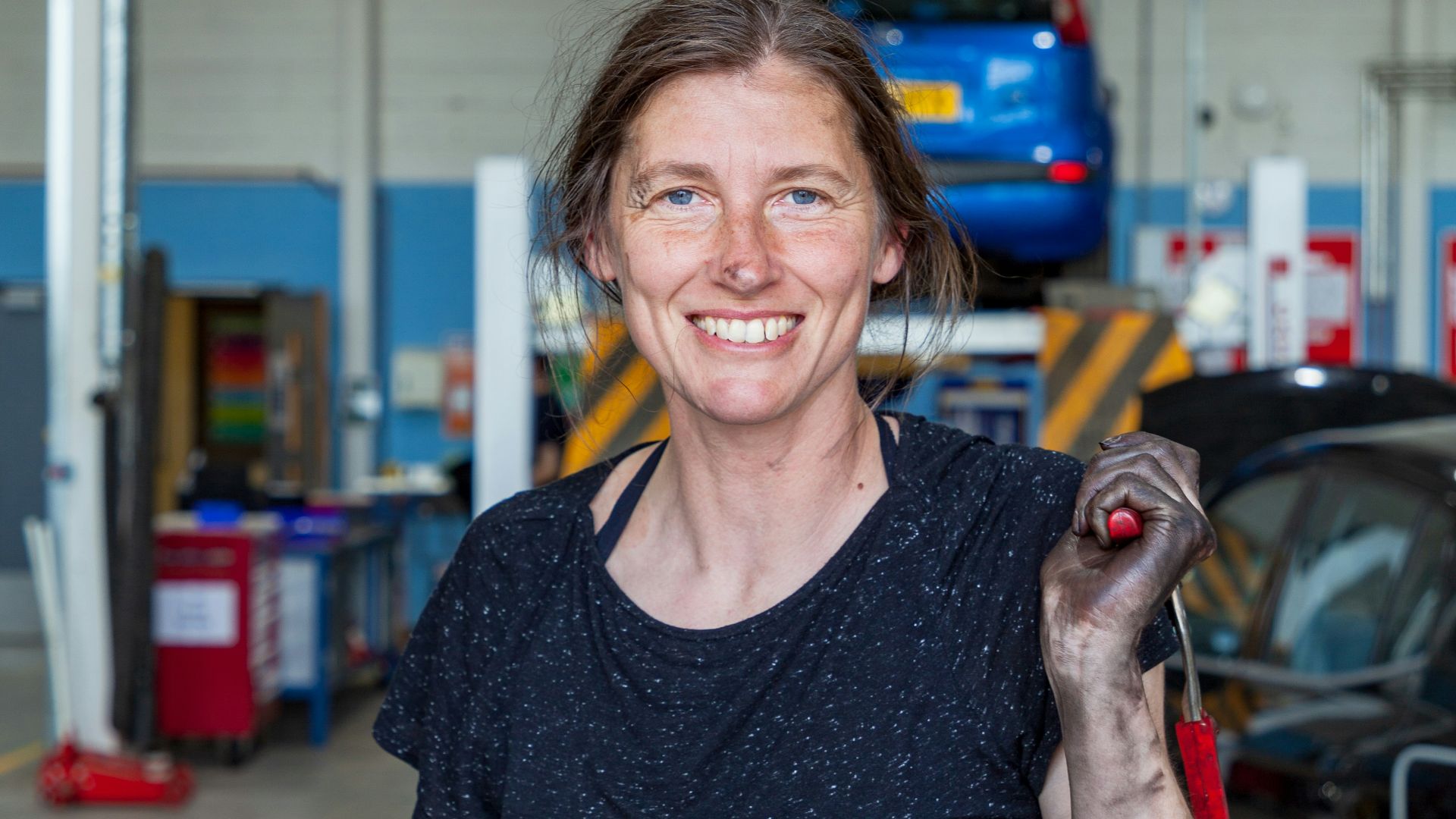 a woman holding a wrench in a garage