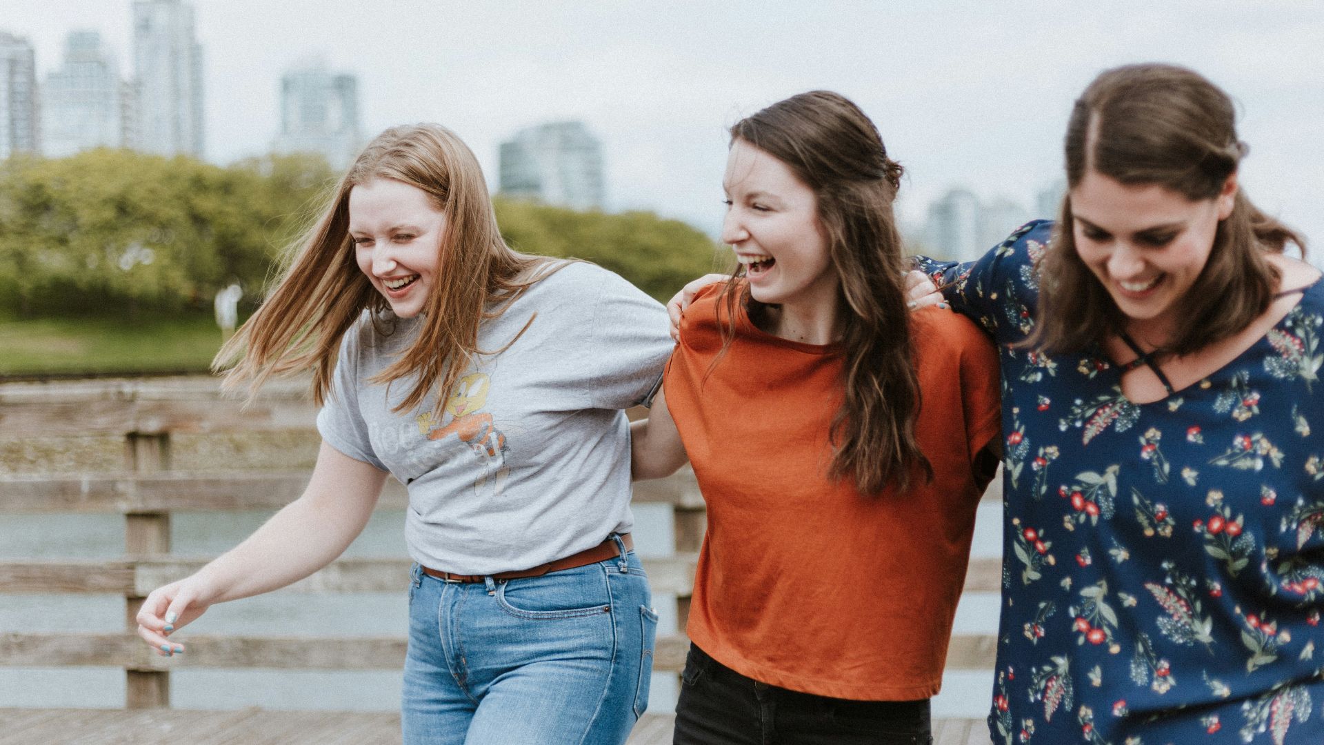 three women walking on brown wooden dock near high rise building during daytime