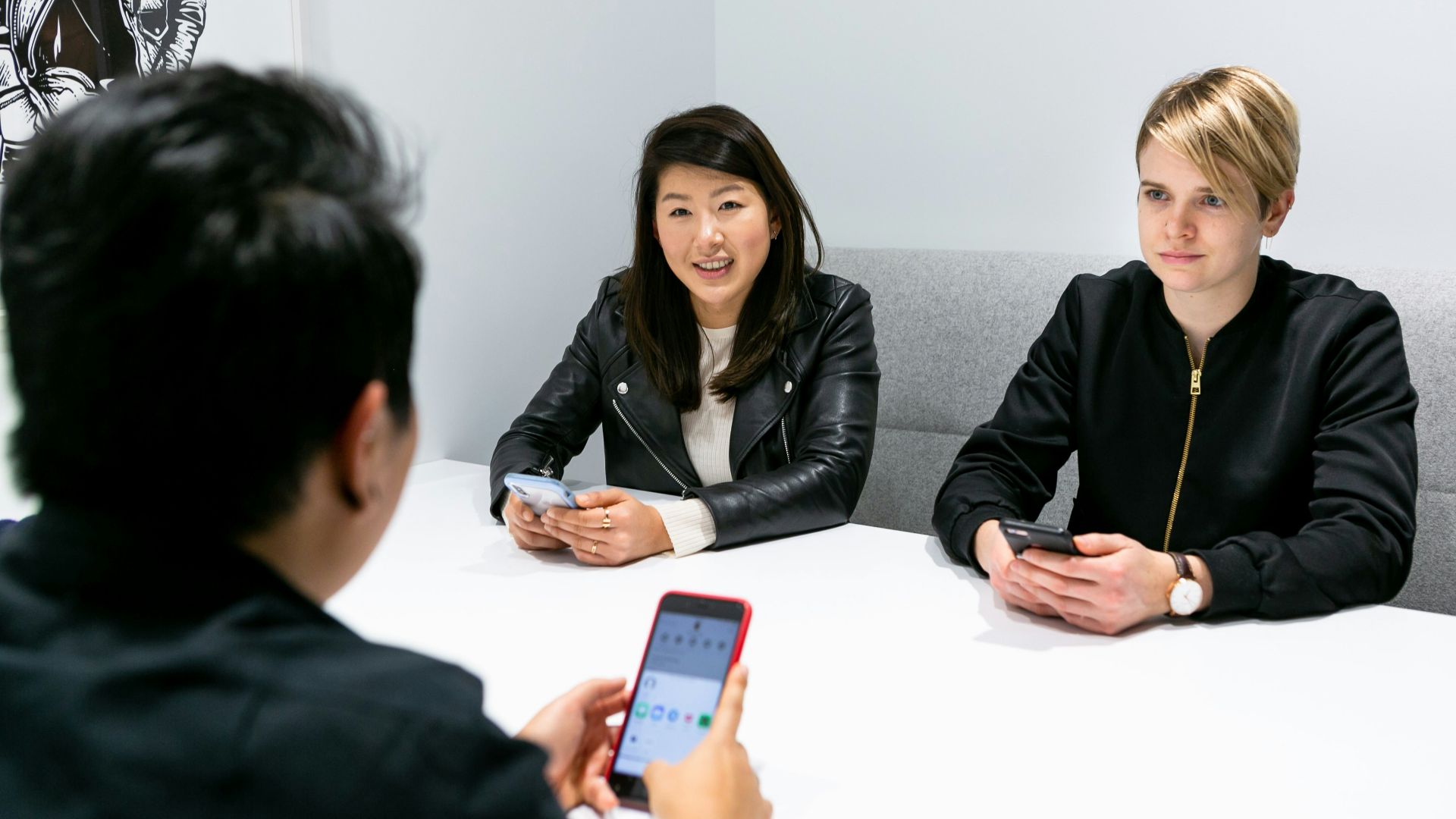 three people in a meeting wearing black jacket holding phones