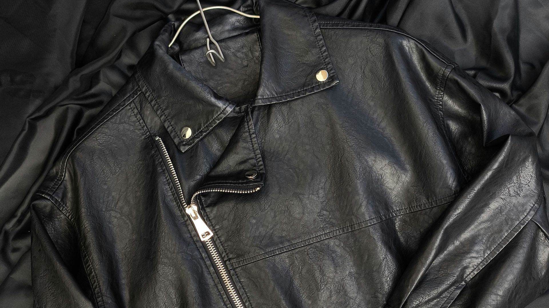 A black leather jacket laying on top of a bed