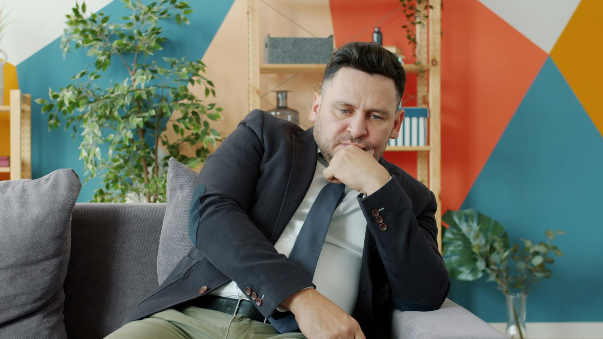 Man in suit sitting on couch looking thoughtful.