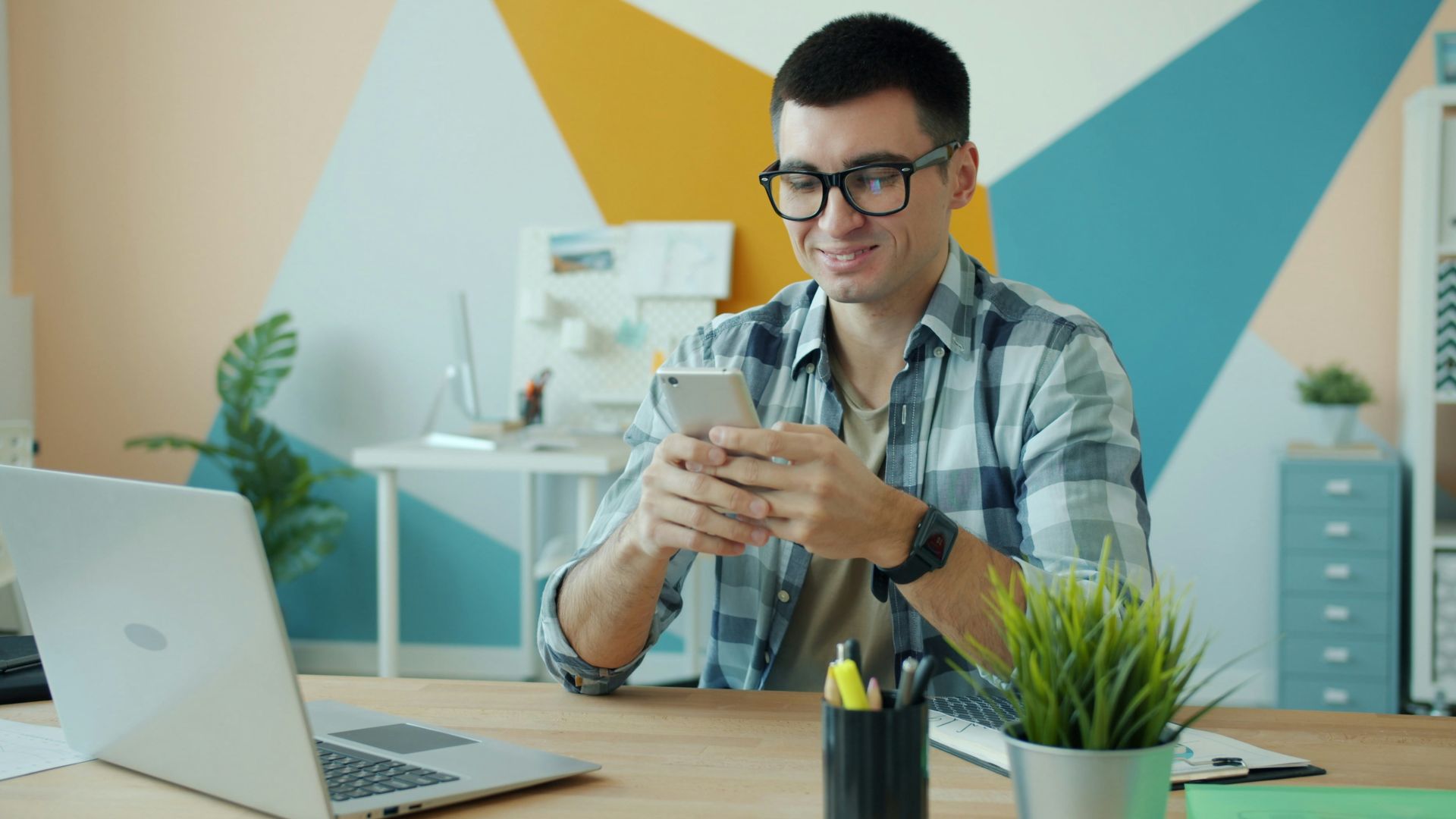 Man in glasses using phone at office desk.