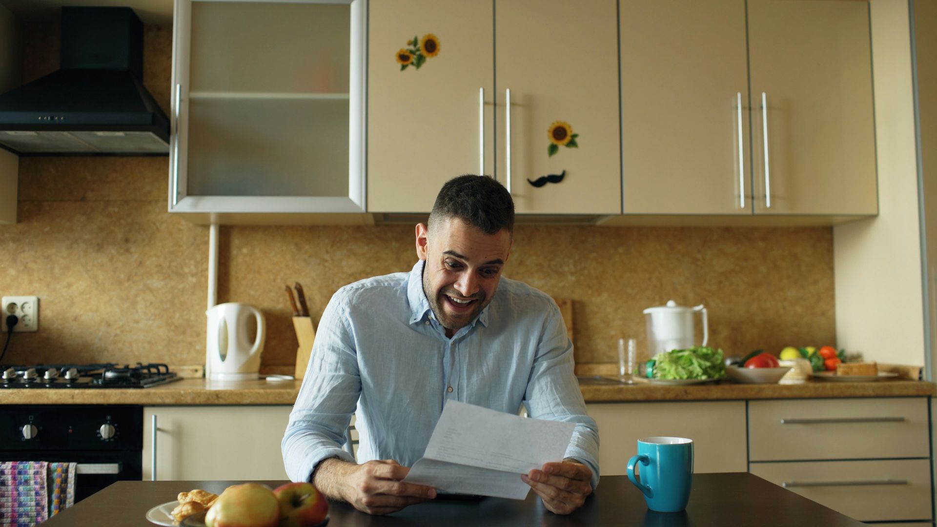Man reading a letter at a kitchen table.