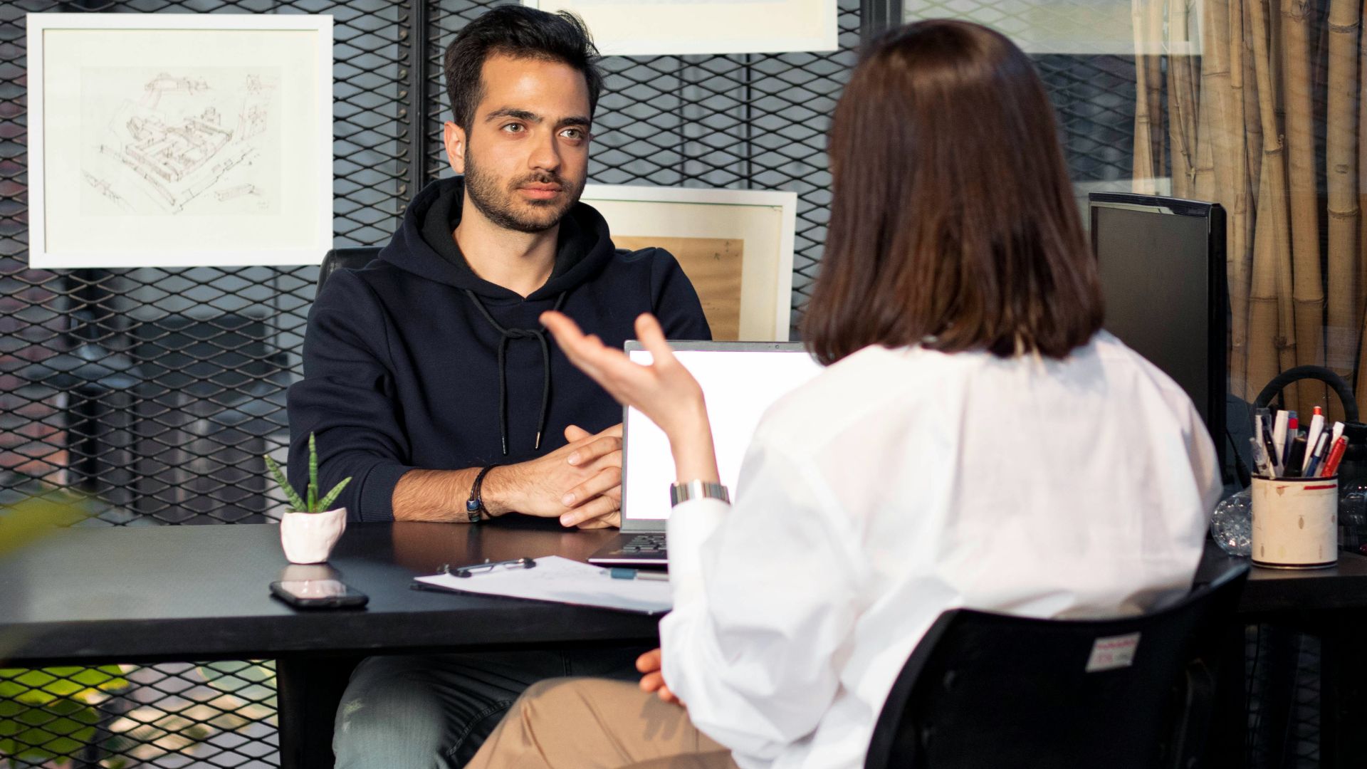 a man sitting at a desk talking to a woman