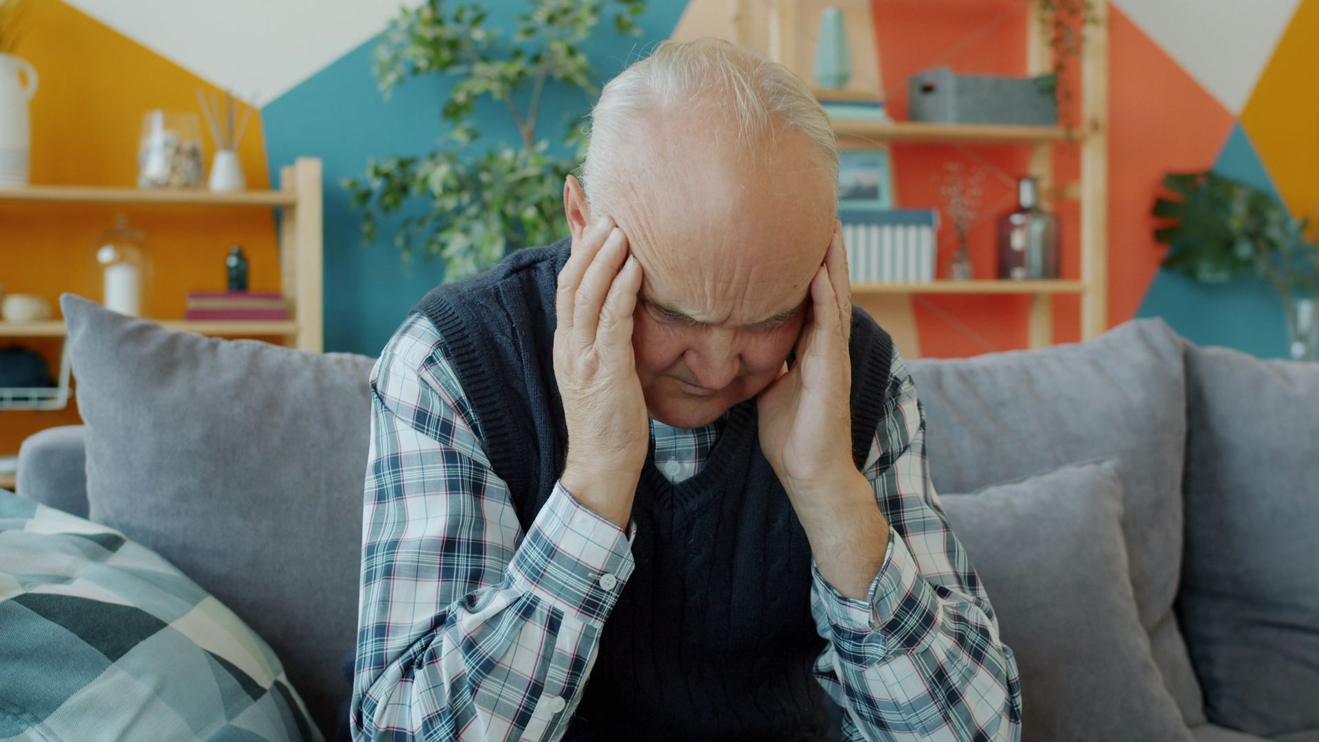 Elderly man holding head in discomfort on couch