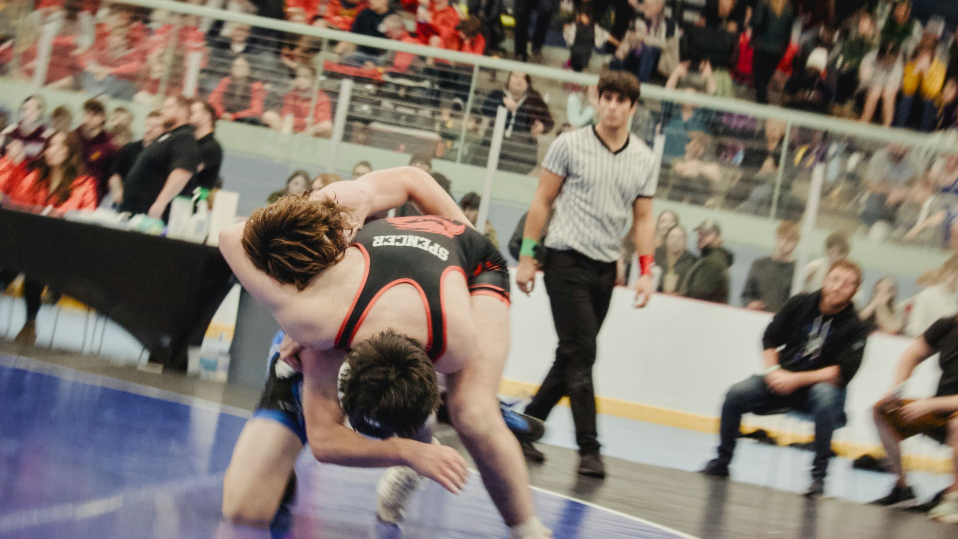 Two wrestlers competing on a mat with referee watching