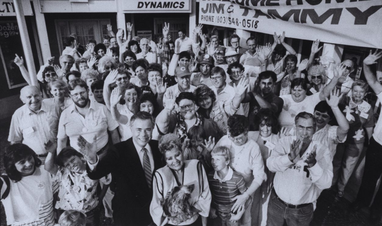 Gettyimages - 50462266, James Bakker [& Wife];James Bakker [Misc.] Disgraced televangelist James Bakker w. wife, Tammy who is holding pet dog as they pose w. a group of waving supporters gathered in front of their office to welcome them home.  