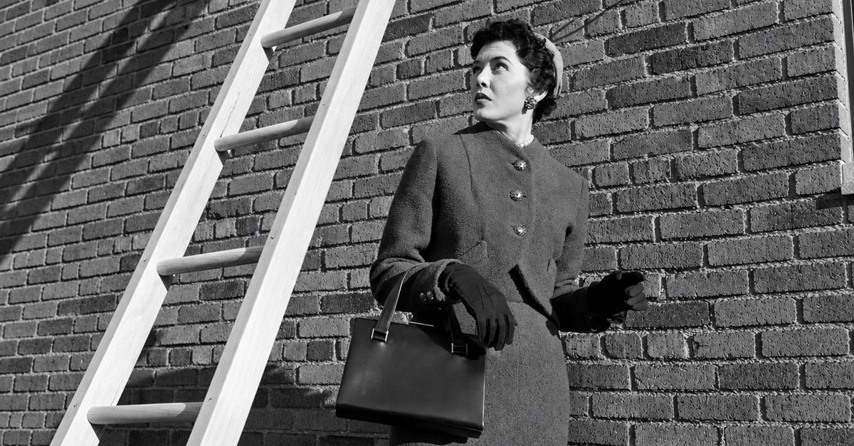 1950s provoking bad luck woman wearing suit and hat carrying handbag walking under ladder