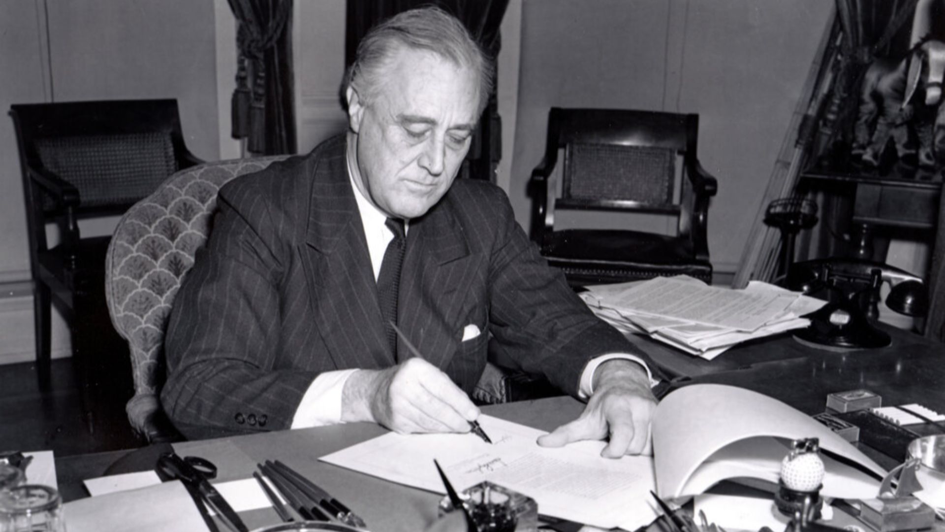President Franklin D. Roosevelt, half-length portrait, seated at desk, looking down, signing H.R. 1776, the lend-lease bill to give aid to Great Britain, China and Greece.