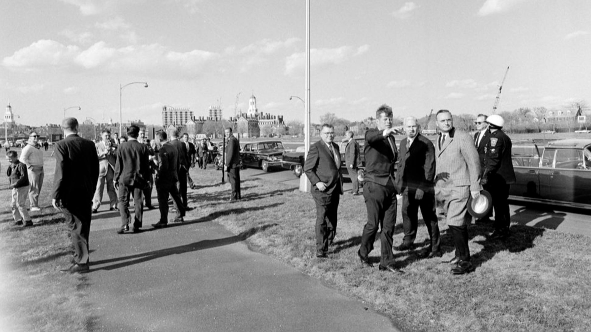 President John F. Kennedy motions with his arm towards the proposed site of his future Presidential Library, along the banks of the Charles River in Boston, Massachusetts. Standing with President Kennedy at right: Archivist of the United States, Dr. Wayne