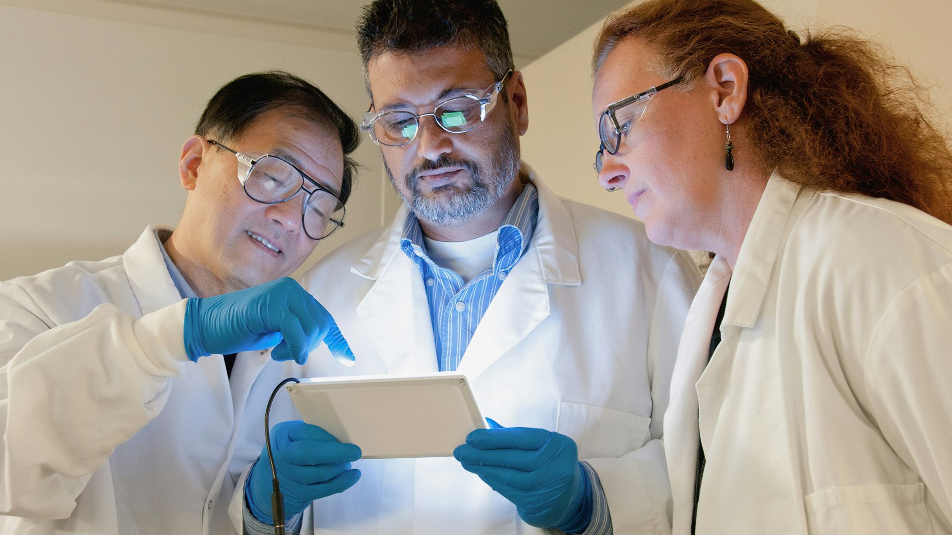 three people in lab coats looking at a tablet