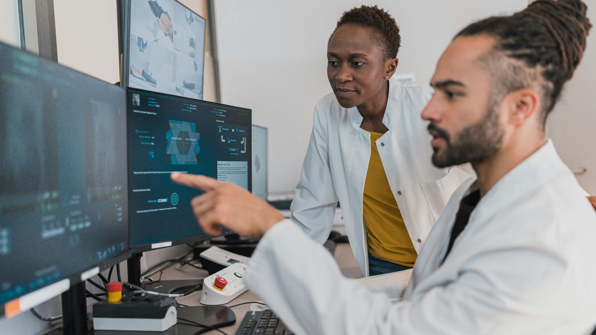 Two medical professionals in white coats reviewing digital imaging on computer monitors