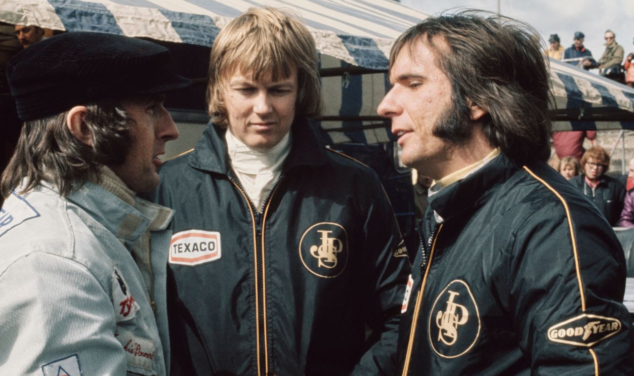 British racing driver Jackie Stewart in conversation with Swedish racing driver Ronnie Peterson (1944-1978) and Brazilian racing driver Emerson Fittipaldi, both wearing Team Lotus overalls, during practice for the 1973 BRDC International Trophy, at the Silverstone Circuit in Silverstone, Northamptonshire, England, 6th April 1973. The 25th British Racing Drivers' Club (BRDC) International Trophy, a non-championship Formula One race, was held on 8 April 1973.