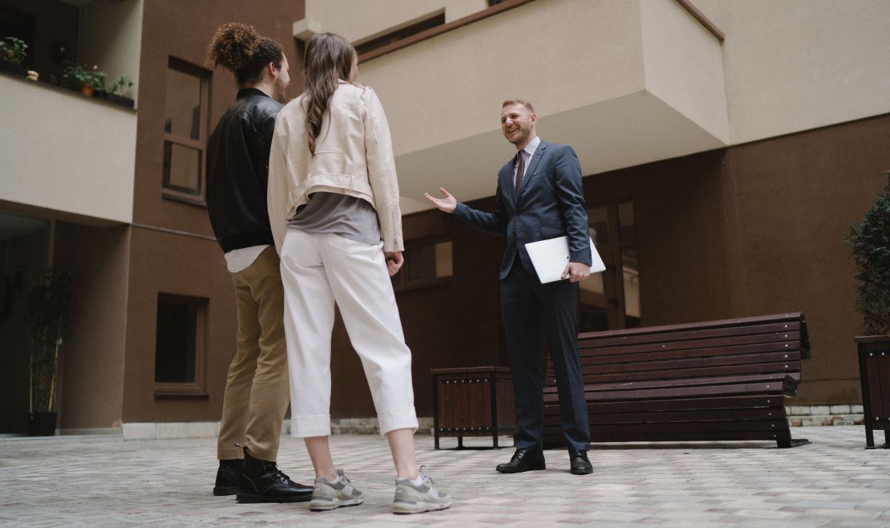 A realtor converses with a couple in a modern apartment courtyard.