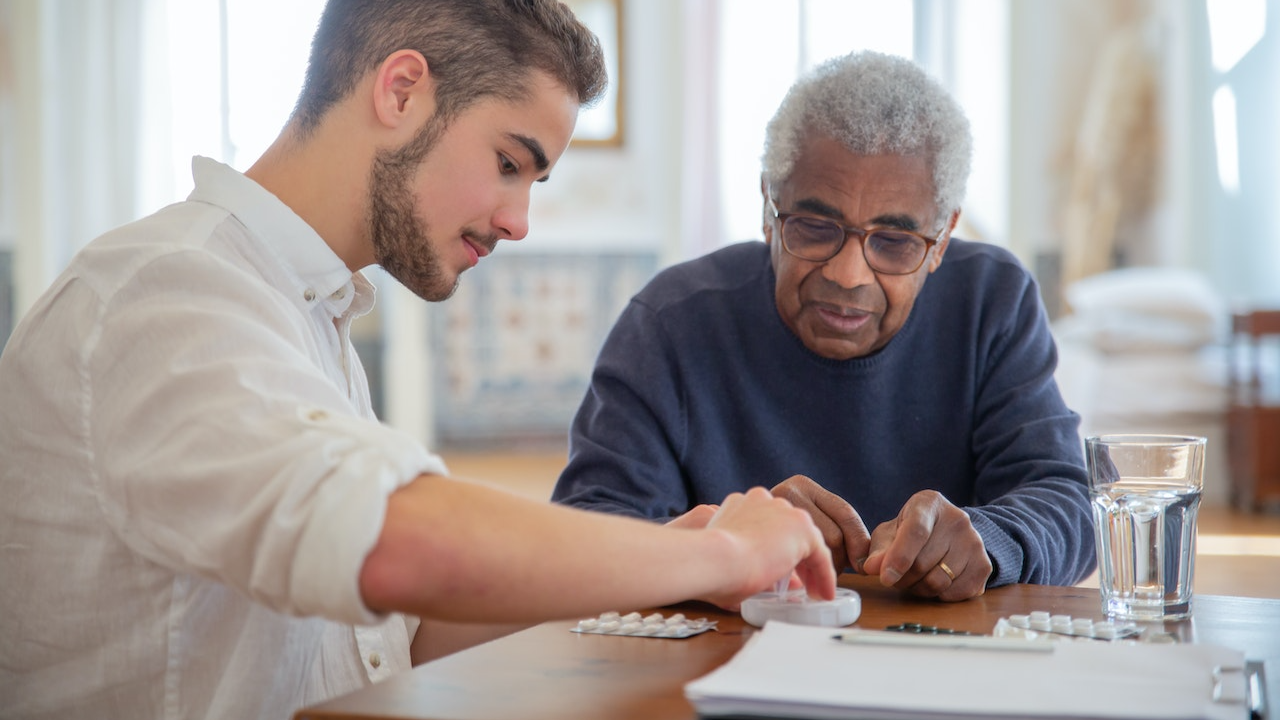 Young man is giving medications to an old man on the table.