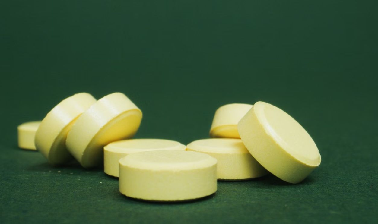 A close-up of scattered yellow tablets on a green surface, emphasizing their color and shape