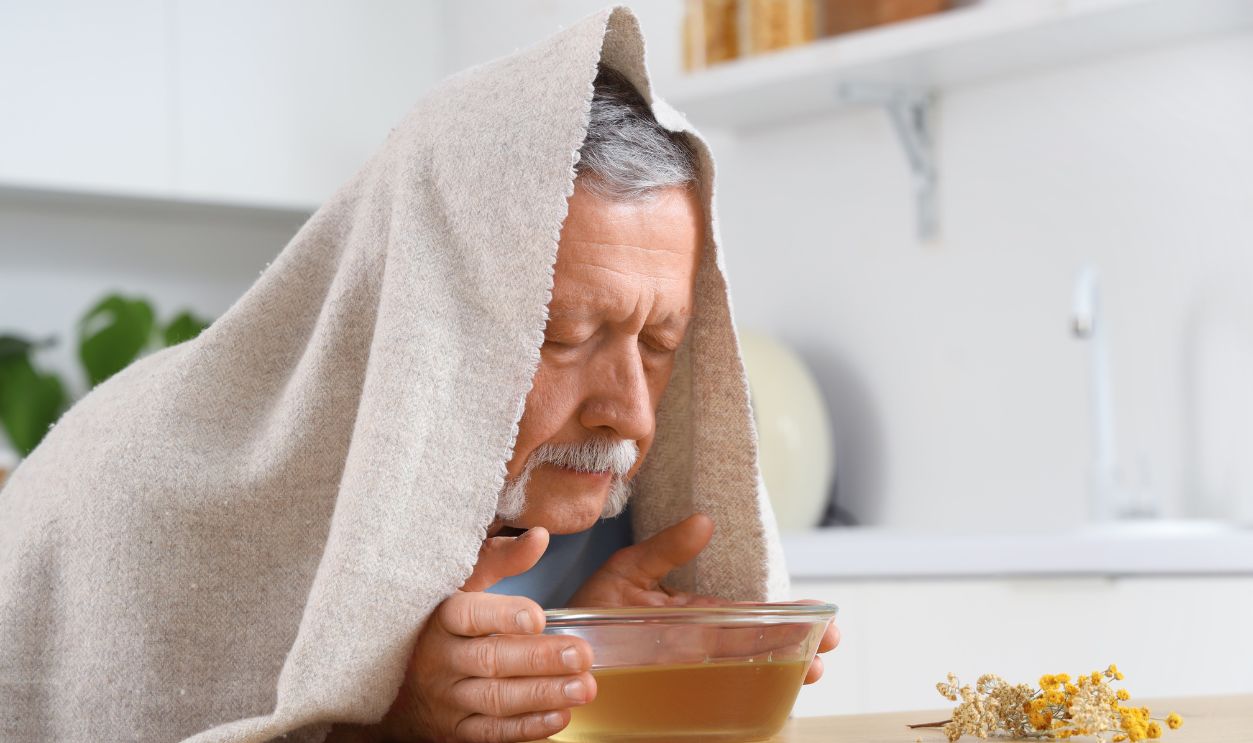 Shutterstock - 2450016937 - Mature man with towel doing steam inhalation at table in kitchen.