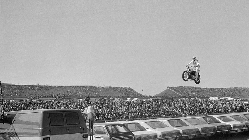 Motorcycle stunt man Evel Knievel sails over a line of 19 automobiles