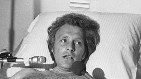 Stunt performer Evel Knievel gives interviews from his hospital bed