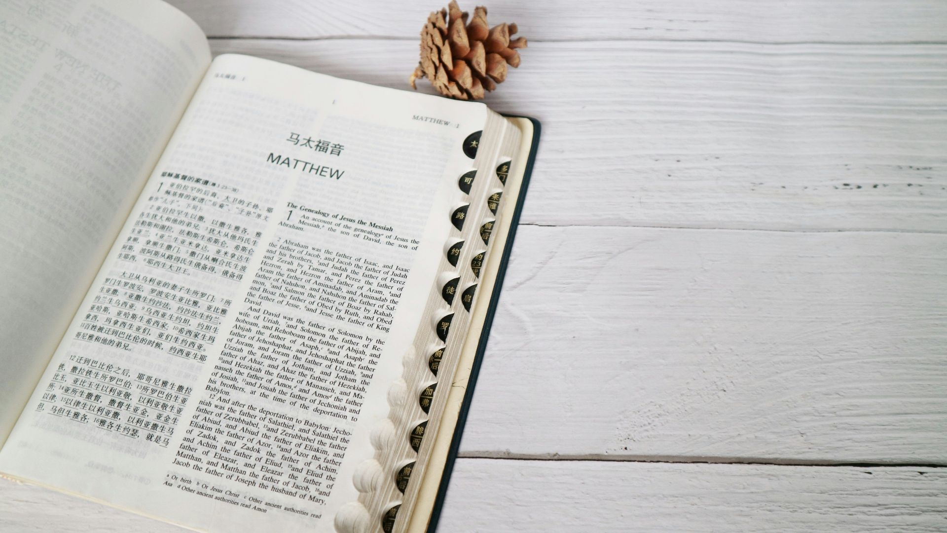 Open Bible displaying the Book of Matthew on a wooden surface with a pine cone accent.