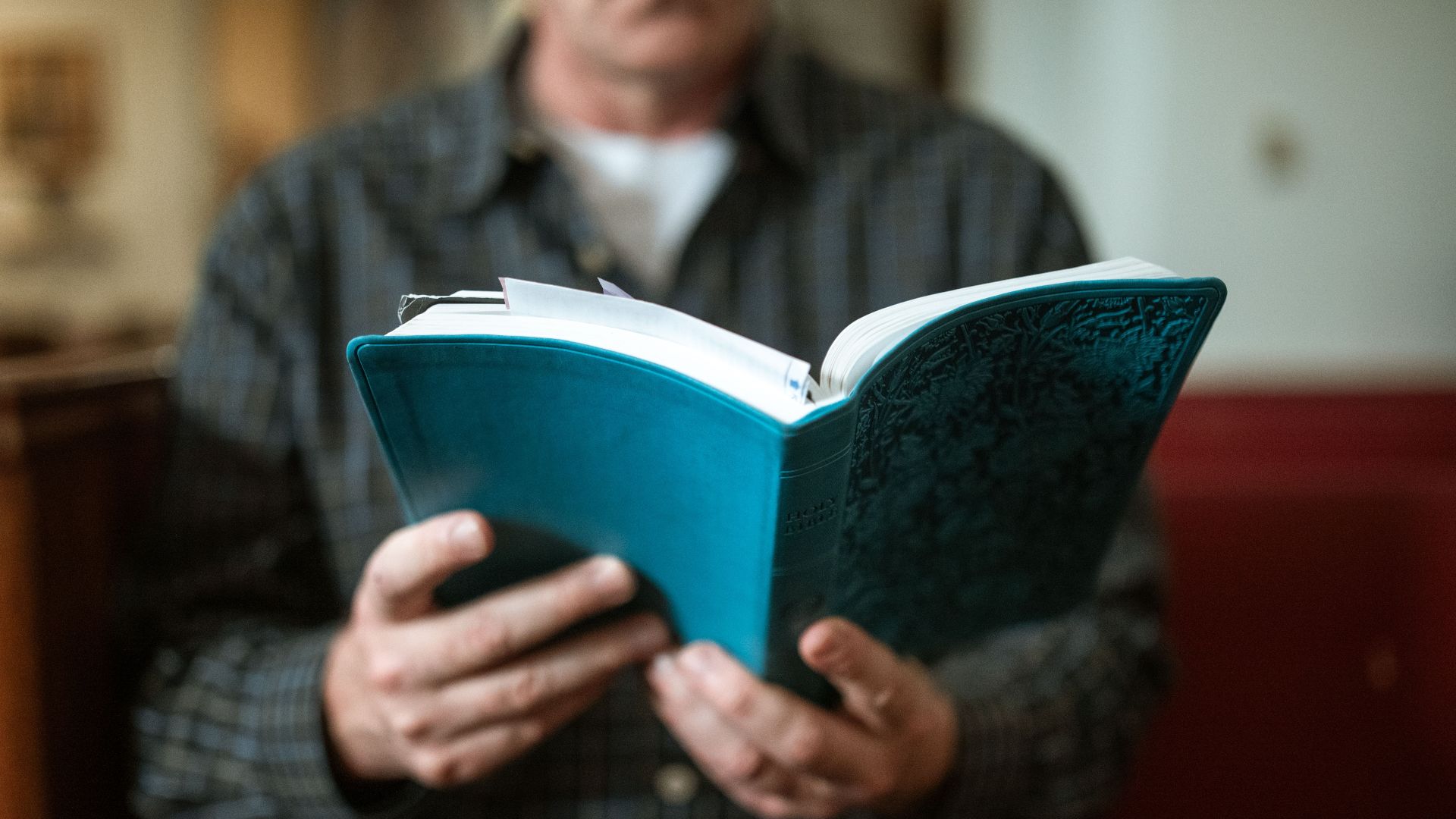 Adult man holding and reading a religious book inside a church.