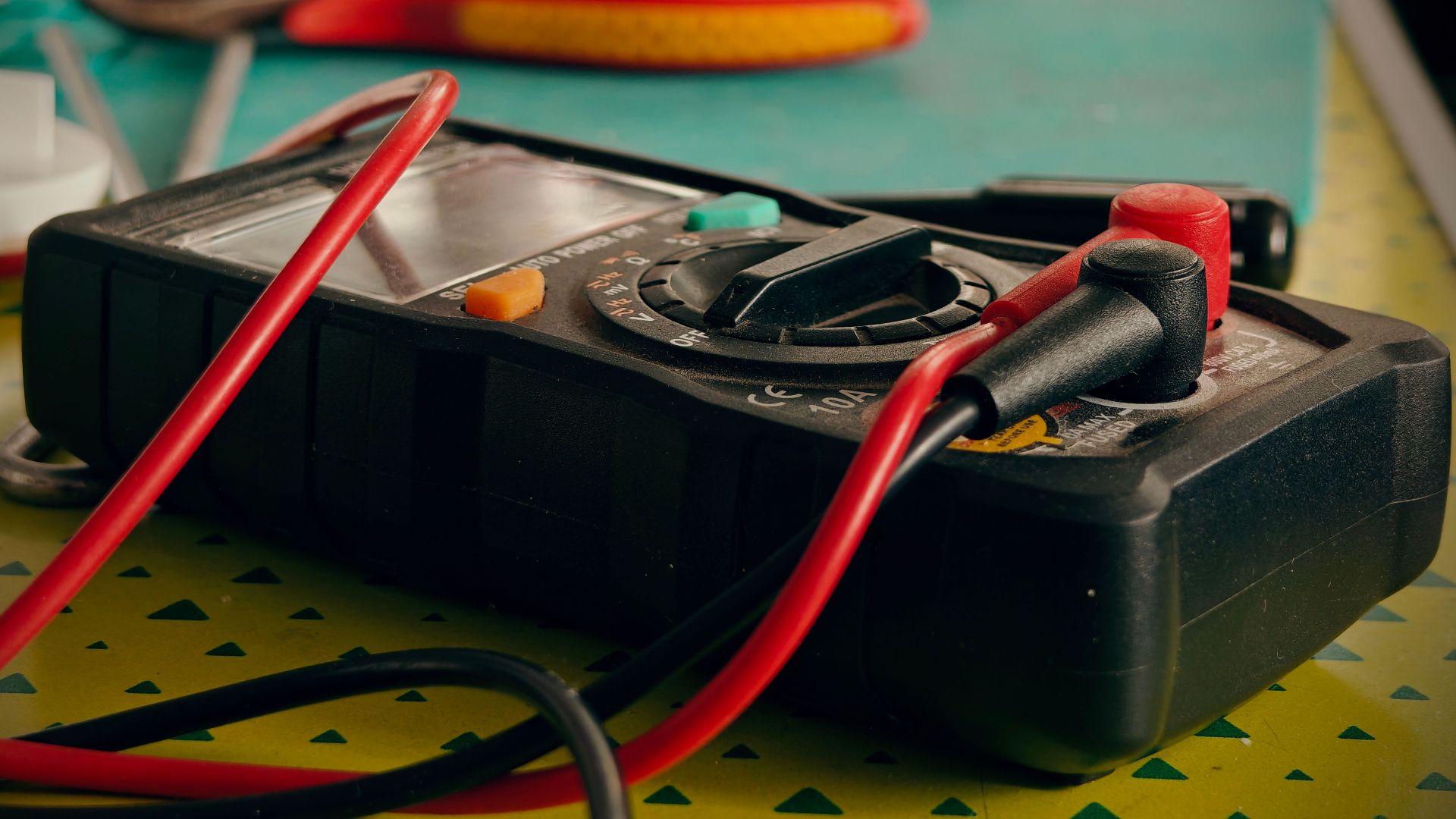 Close-up view of a multimeter and various tools on a workspace table.