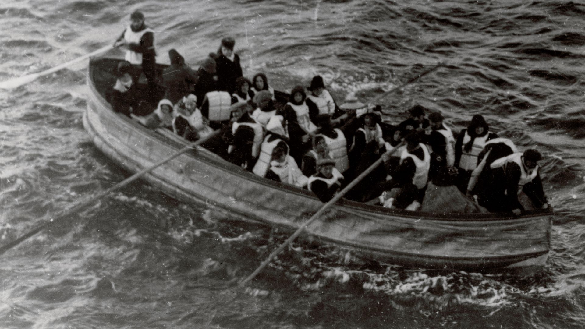 This is a photograph, a lifeboat carrying Titanic shipwreck survivors, serves as an exhibit in the case. The following partial caption, which is faded and difficult to read, appears on the back of the fractured mat: