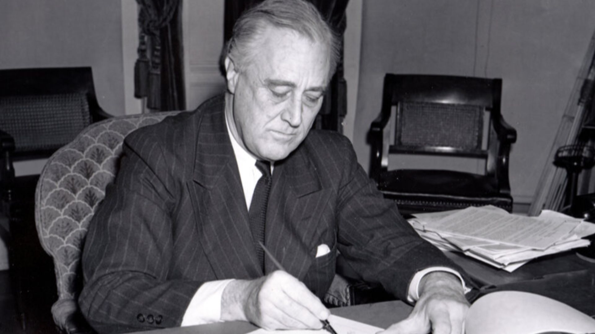 President Franklin D. Roosevelt, half-length portrait, seated at desk, looking down, signing H.R. 1776, the lend-lease bill to give aid to Great Britain, China and Greece.